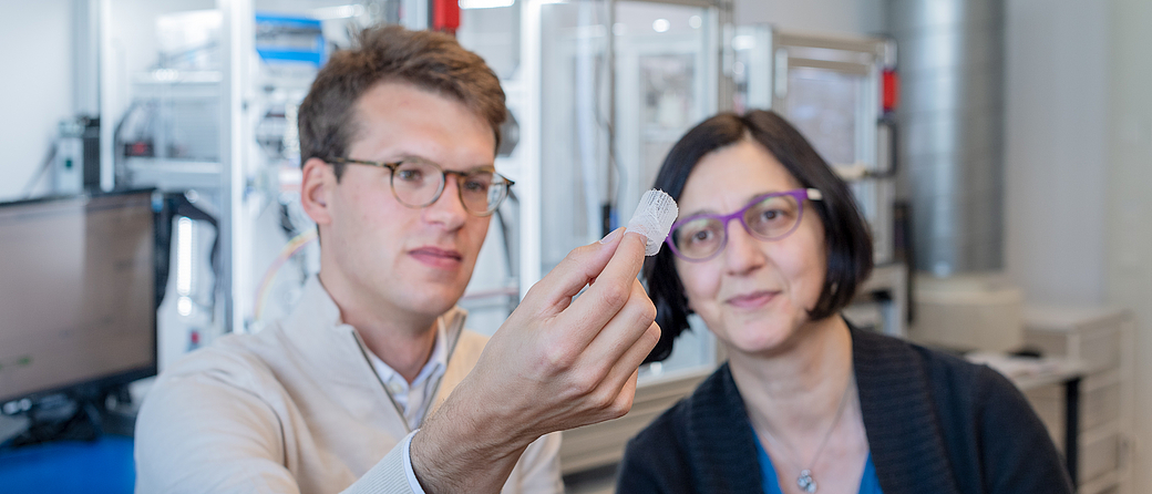 Petra Mela, Professor of Medical Materials and Implants at the Technical University of Munich (TUM) and doctoral candidate Kilian Meuller examine an artificial heart valve produced with the additive manufacturing technology melt electrowriting. Image: Andreas Heddergott / TUM
