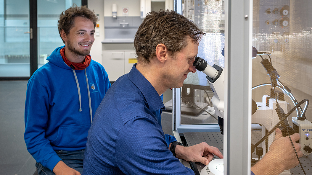Prof. Bernhard Wolfrum (vorn) und Lukas Hiendlmeier prüfen die Elektroden unter dem Mikroskop auf ihre elektrische und mechanische Funktionalität. Bild: Andreas Heddergott / TUM